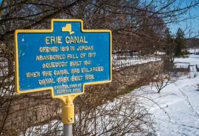 A commemorative plaque documents the history of the Erie Canal: Opened in 1819, abandoned fall of 1917, an extra aqueduct built in 1841 to expand the canal, and a canal park built in 1932.