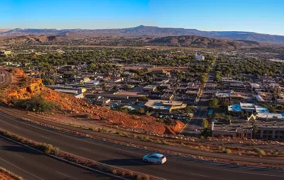 Aerial view of St. George, Utah at sunset with road in foreground and red mountains in background.