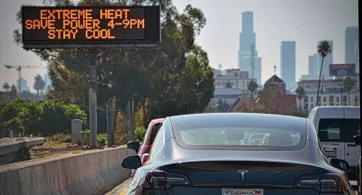 Cars in traffic jam on Los Angeles highway with road sign in center median warning of extreme heat.