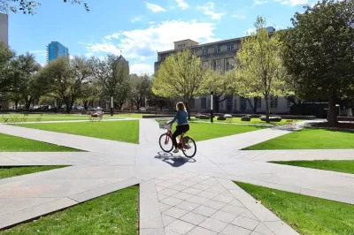 Woman rides bike on paved walkway through plaza in Fort Worth, Texas.