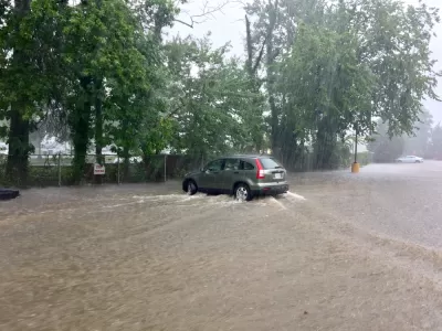 A sports utility vehicle drives throw brown floodwaters that have inundated the entire area depicted in the picture.