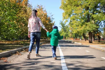 Parent and child walking, holding hands on mixed-use trail with trees