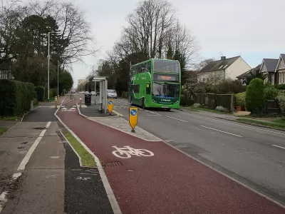 Red painted bike lane next to floating bus stop and green double-decker bus in the UK.