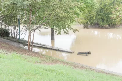 The trees, benches, and other landscape elements of a park are submerged in brown flood waters.
