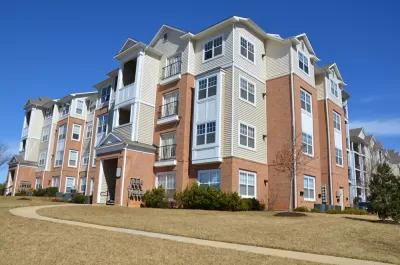 A large, four-story apartment building is surrounded by grass and concrete walkways. 