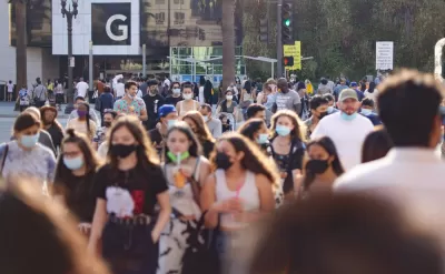 Large numbers of young people, some wearing and masks and others note, walk around an outdoor shopping mall in Southern California.