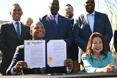 Governor Wes Moore of Maryland holds up executive order while sitting at table surrounded by smiling officials.