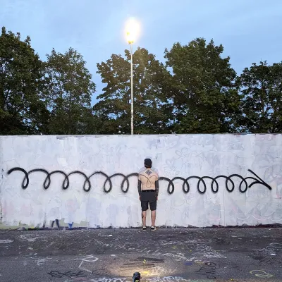 Man standing in front of white wall with black graffiti paint spiral running horizontally across.