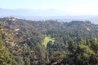 The fairway of a golf course is visible amidst the rolling hills of Griffith Park above Los Angeles.