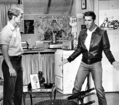 Black and white still from Happy Days showing Fonzie and Richie standing in Fonzie's garage apartment.
