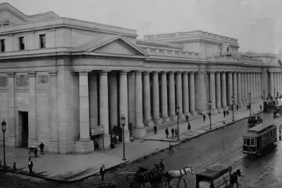 An image of historic Penn Station when it was first built in 1910, viewed from the outside with people, carriages, and streetcars passing by.