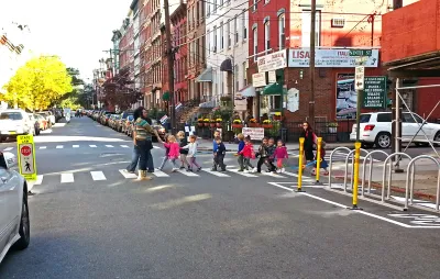 Group of children with crossing guard crossing the street at a marked crosswalk in Hoboken, New Jersey on street with brick walk-up buildings.