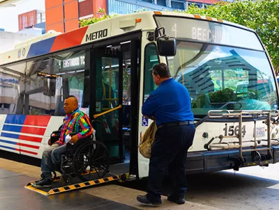 Man in wheelchair exiting public bus on ramp while operator waits outside in Houston, Texas.