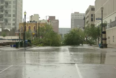 Flooded street and two downed trees with downtown Houston buildings in background