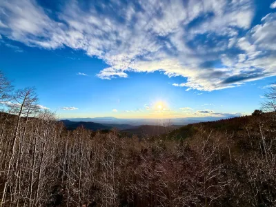 Sun rising over mountain forest with bright blue sky.