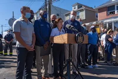 New York politicians, including Governor Kathy Hochul and Mayor Bill de Blasio, gather in front of microphones for a press conference.