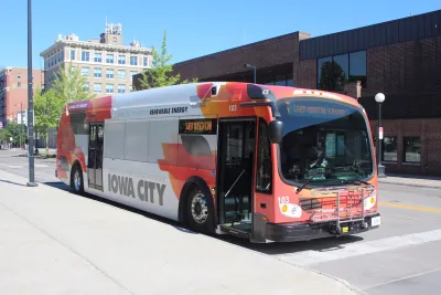 Red and white Iowa City Transit bus stopped next to a curb.