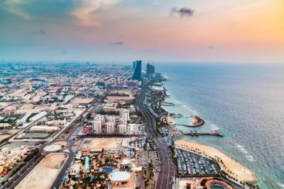 An aerial view down the length of the Jeddah coastline in Saudi Arabia, showing coastal developments, beaches, and a few high-rise buildings along the shoreline.