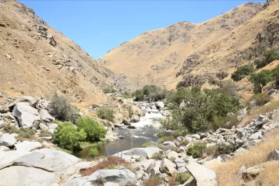 The Kern River passes through a steep river canyon filled with jagged rocks and surrounded by hills of golden grass. 