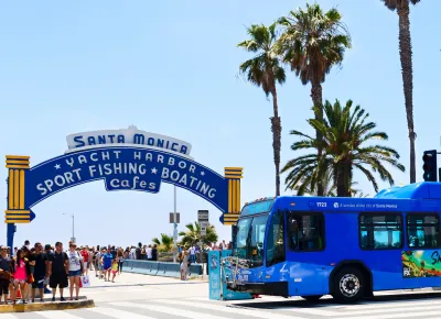 Blue transit bus passing in front of Santa Monica Pier entrance arch on a sunny day.