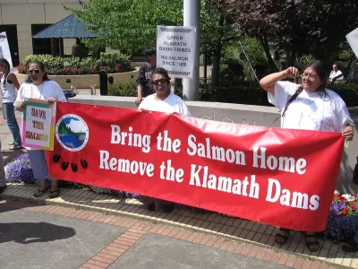 Native demonstrators hold a red banner reading "Bring the salmon home - Remove the Klamath Dams."