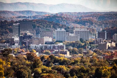 An aerial view of downtown Knoxville, Tennessee, with rolling hills and autumn foliage in the background.