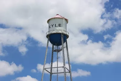 White water tower with KYLE text against blue sky with white clouds.
