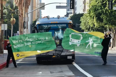 Bus driving through green banner held by two Metro employees at inauguration of new bus lane in downtown Los Angeles.