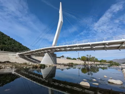 A cable-stayed bridge designed spans the water of the Los Angeles River, which is placid and dotted with rocks.
