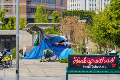 A homeless encampment is set up outside a transit station, next to bike share stations and a ticket dispenser.