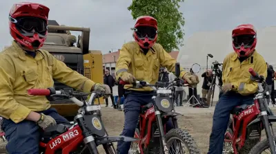 Three firefighter medics wearing yellow jackets and red helmets sitting on red LAFD electric motorcycles.
