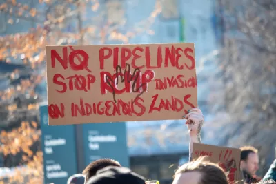 A sign held above the crowd at a protest reads "No Pipelines" and "Stop RCMP Invasion on Indigenous Lands" 