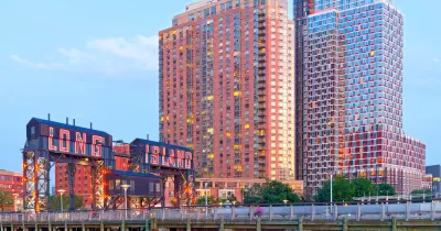 A photo of a bridge reading Long Island City in front of high-rise buildings glittering in a sunset.