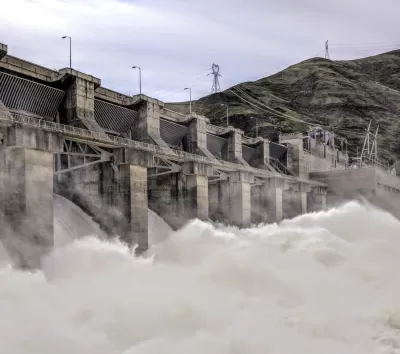 Water rushes over a spillway at a large concrete dam.