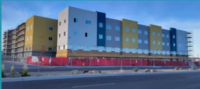 White, yellow, gray boxy apartment building with construction fence surrounding bottom floor in Albuquerque, New Mexico.