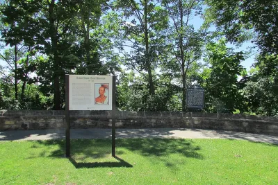 Informational plaque in front of paved walkway next to tall green trees in Black Hawk State Historic Site, Illinois.