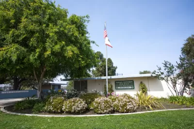 Small white one-story building with Maggie Hathaway Golf Course sign with American flag on flagpole and green lawn