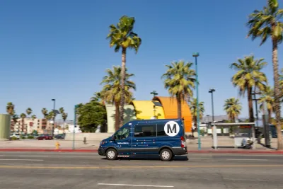 Dark blue shuttle van driving past colorful orange and yellow North Hollywood subway station in Los Angeles, California.