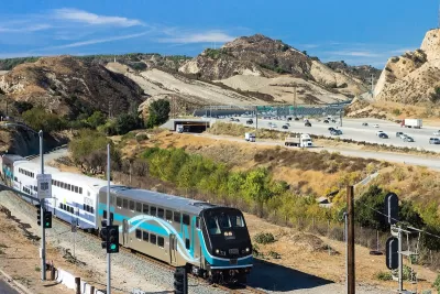 Silver and white Metrolink commuter train passing through Newhall Pass with desert mountains in background in Antelope Valley, California.