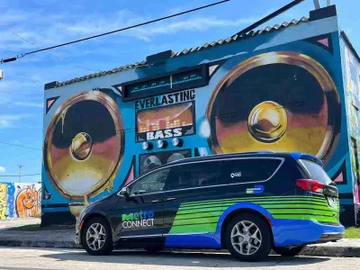 Black and green MetroConnect microtransit van in front of mural of boom box on Miami building.