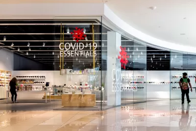 A man passes by a store in an empty mall. A sign in the window of the store reads "Covid-19 Essentials."
