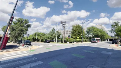 A gray building partially obscured by trees, behind a four way intersection.