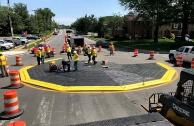 Workers in safety vests installing a black modular roundabout ringed with yellow.