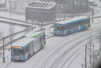 Two buses pull up to a station on a snowy day.