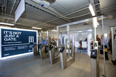 New fare gates with clear panels with people standing behind them in NYC subway station.
