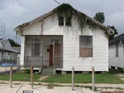Small white wood house with boarded up windows in New Orleans, Louisiana with moss growing down from roof.