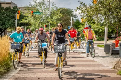 Group of people riding Pacers Bikeshare bikes on a tree-lined paved path.