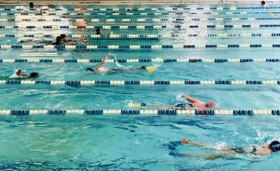 People swimming in an indoor lap pool with blue and white lane dividers.