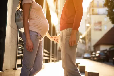 A pregnant woman holds hand with a man in an urban setting.
