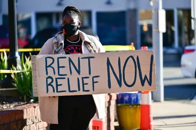 Person holding sign reading 'Rent Relief Now!' wearing blue face mask.